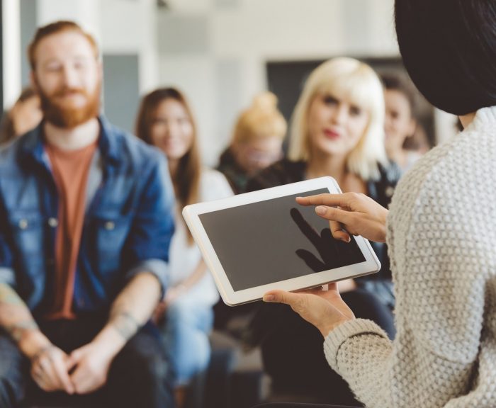 Woman holding tablet, presenting to seated audience